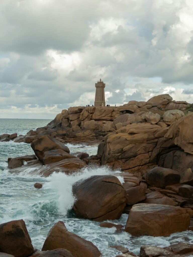 The Côte de Granit Rose (Pink Granite Coast) in Brittany, France, showing a white lighthouse perched on dramatic pink-hued granite cliffs overlooking the vibrant turquoise sea, ideal for serene adults-only luxury travel.