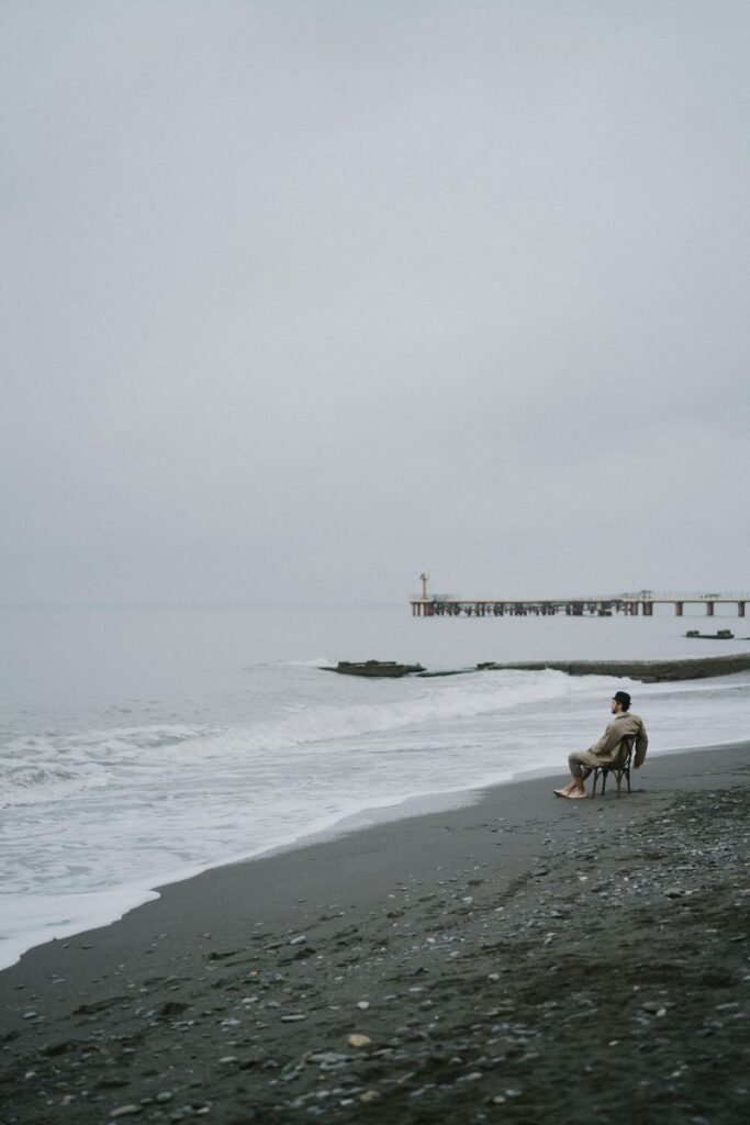 Adult sitting on a beach chair reflecting near the water during the day.